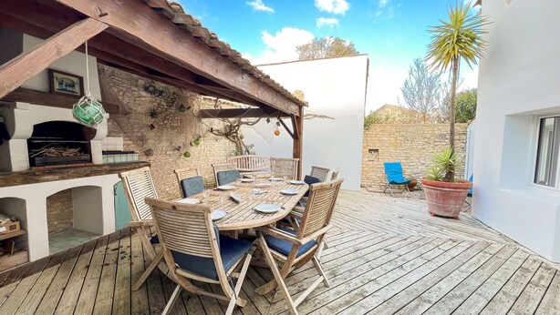 An outdoor dining area with a wooden table and chairs, a stone wall, and a view of the surrounding landscape. - Charming villa in the center with courtyard (LA COUARDE SUR MER)