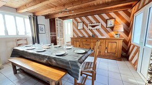 A dining area with a wooden table set for six, a bench, and a wooden cabinet with a herringbone-patterned wall behind it. - Charming villa in the center with courtyard (LA COUARDE SUR MER)