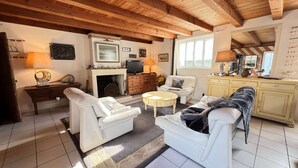 A cozy living room with a fireplace, white furniture, and wooden beams on the ceiling. - Charming villa in the center with courtyard (LA COUARDE SUR MER)