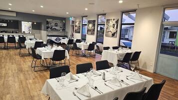 A restaurant with multiple tables set for dining, featuring a modern interior with wooden flooring and large windows offering views of the outside.