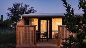 A wooden deck with a table and chairs, a sliding glass door, and a fenced area. - Kennedy Park Resort (Napier)