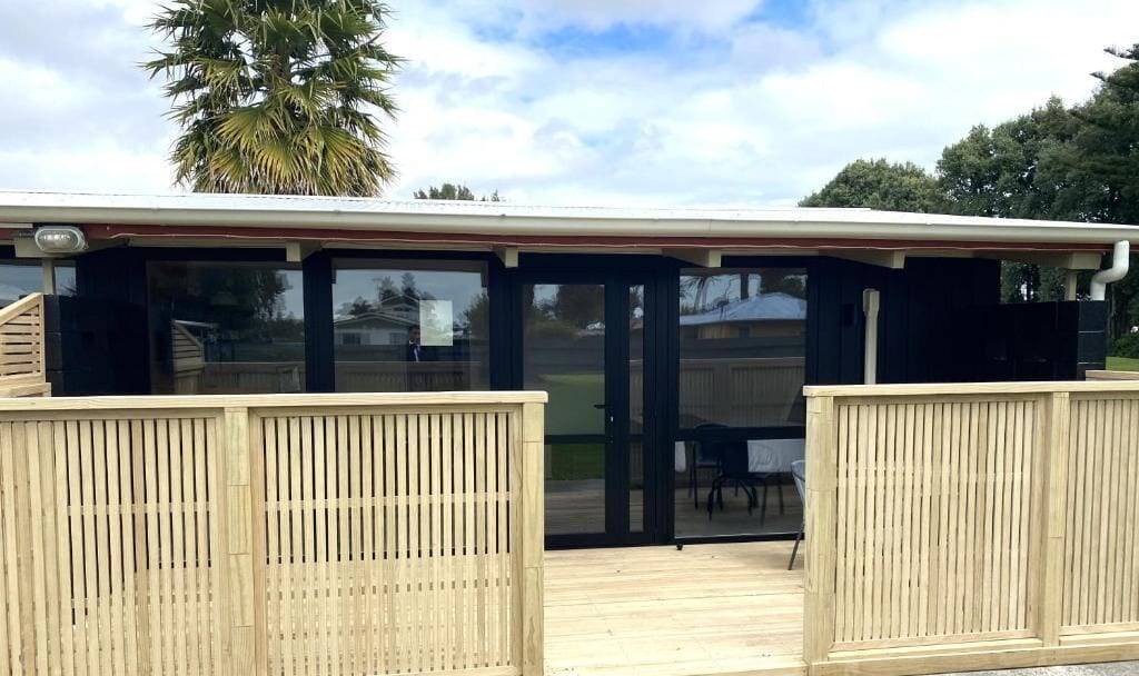 A covered outdoor area with a wooden deck and glass doors leading to an interior space.