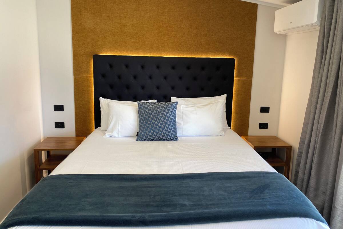 A neatly made bed with a dark headboard, white pillows, and a blue patterned pillow.
