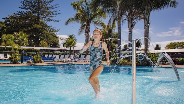 A pool with clear blue water, surrounded by lounge chairs and palm trees. - Kennedy Park Resort (Napier)
