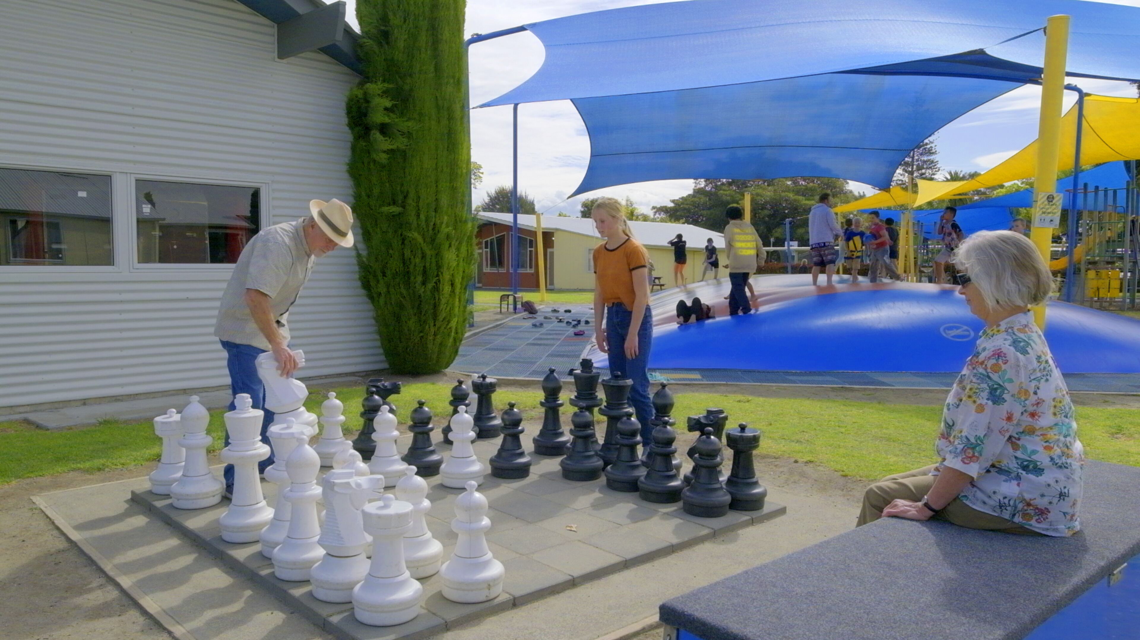 A chessboard set up outdoors with people playing.