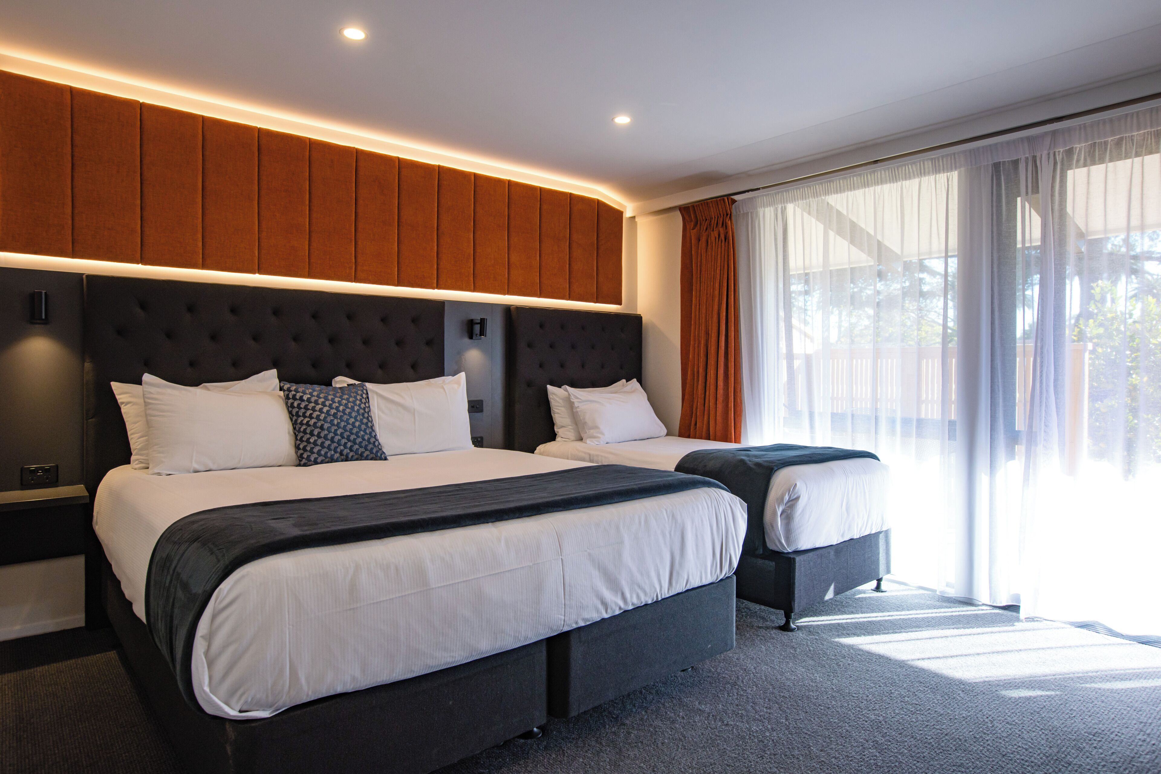 Una habitación de hotel moderna con dos camas, un ventanal con cortinas y una lámpara fijada a la pared.