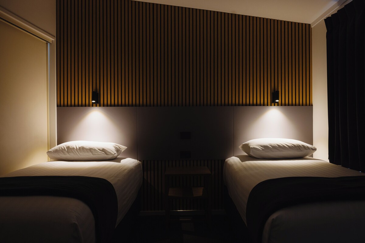 Una habitación de hotel con dos camas, cabecera de madera con listones y lámparas de noche.