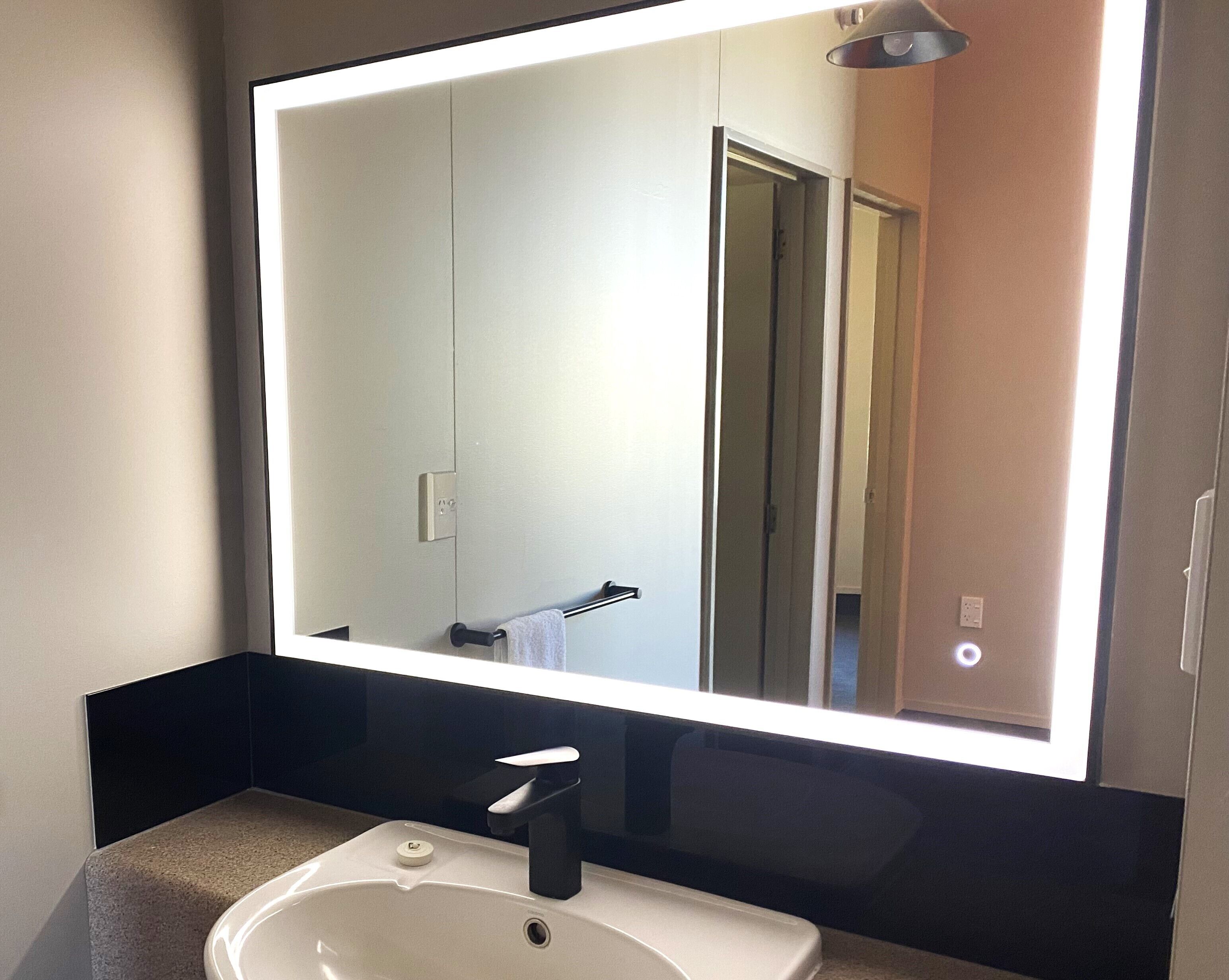 A bathroom with a large mirror, a sink, and a towel rack.