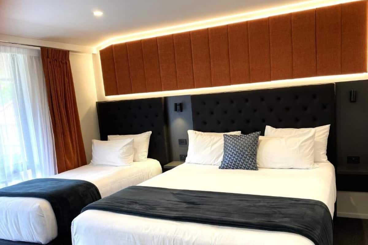 A hotel room with two beds, a large padded headboard, and a modern light fixture.
