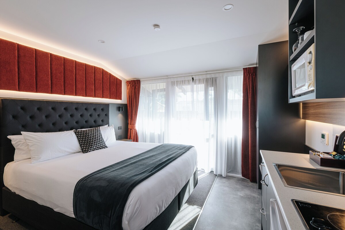 A modern hotel room with a large bed, a built-in desk, a microwave, and a view of the city.