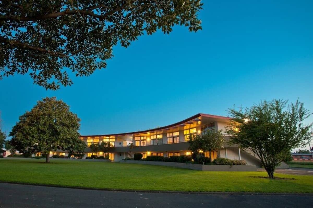 A modern building with a curved roofline, surrounded by well-maintained lawns and trees.