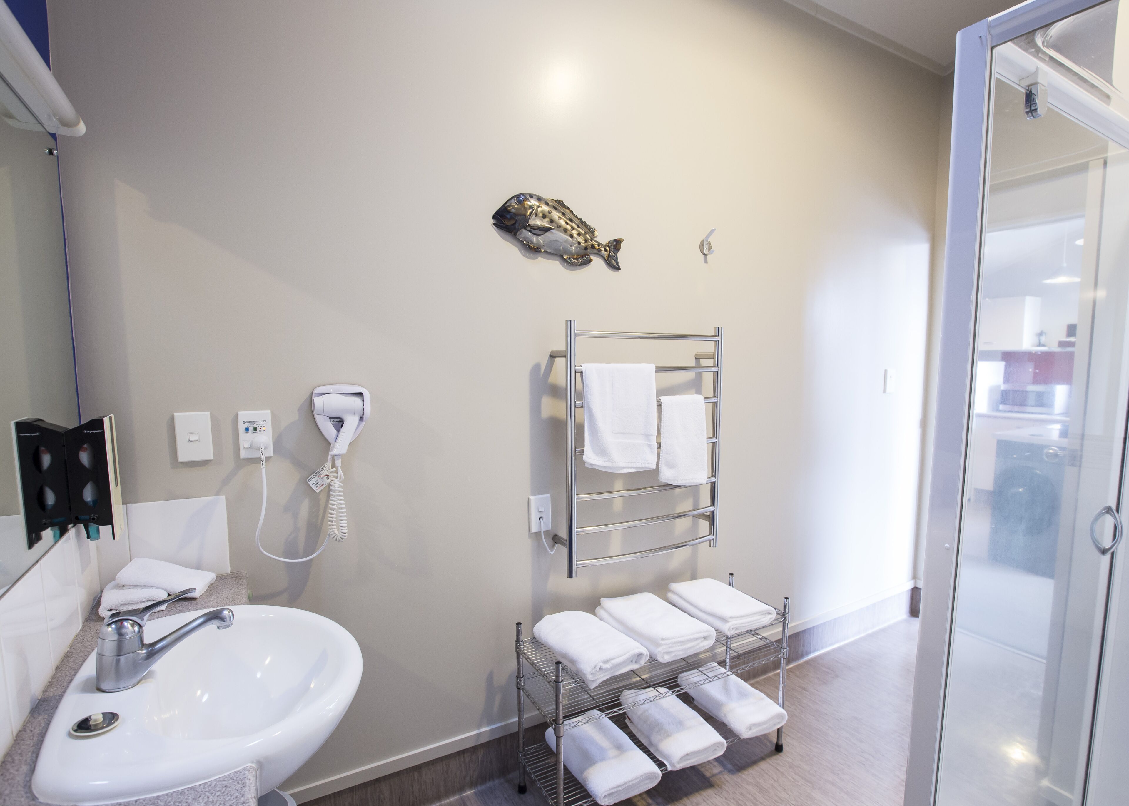 A bathroom with a sink, a hairdryer, a towel rack with towels, and a fish decoration on the wall.