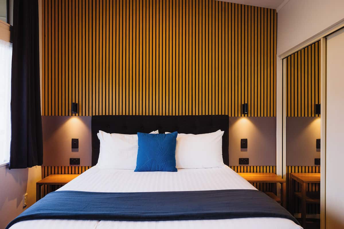 A hotel room with a large bed, a wooden headboard, and a wall with vertical wooden slats.