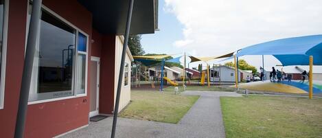 A playground area with slides and climbing structures, a building with a red facade, and a covered seating area.