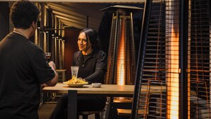 A dining table with a plate of food and a drink, a person seated, and a standing individual. - Kennedy Park Resort (Napier)
