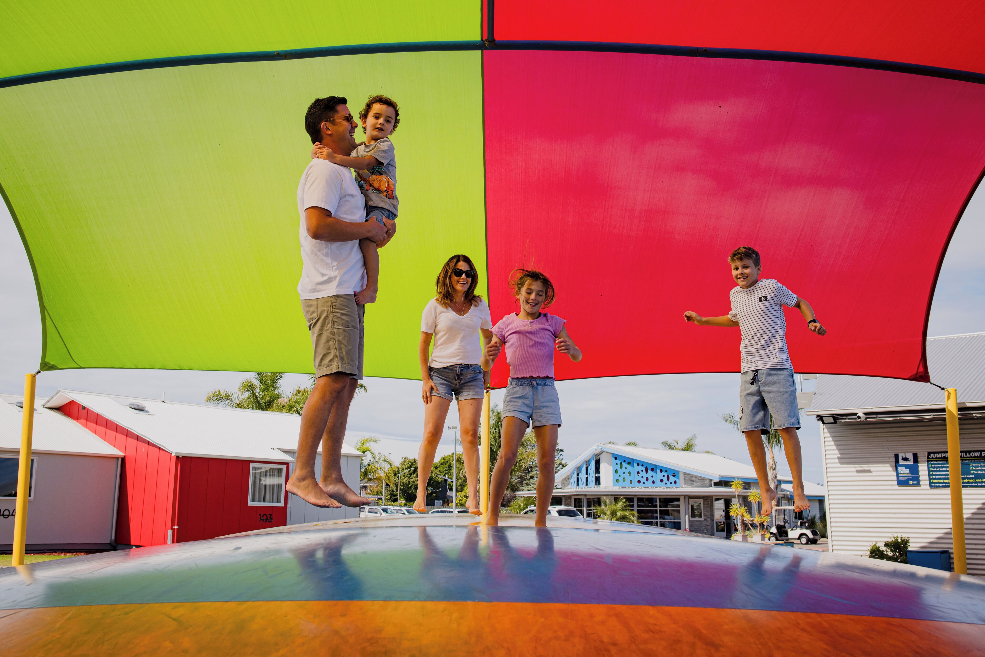 Un trampoline surmonté d’une toile colorée et entouré d’un bâtiment à la façade rouge et blanche.