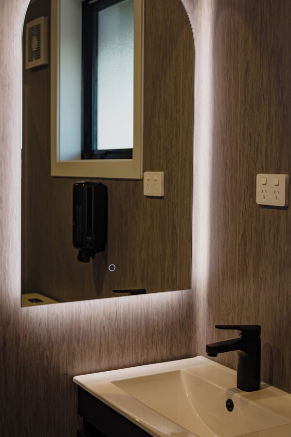 A bathroom with a white sink, a black faucet, a mirror, and a soap dispenser.