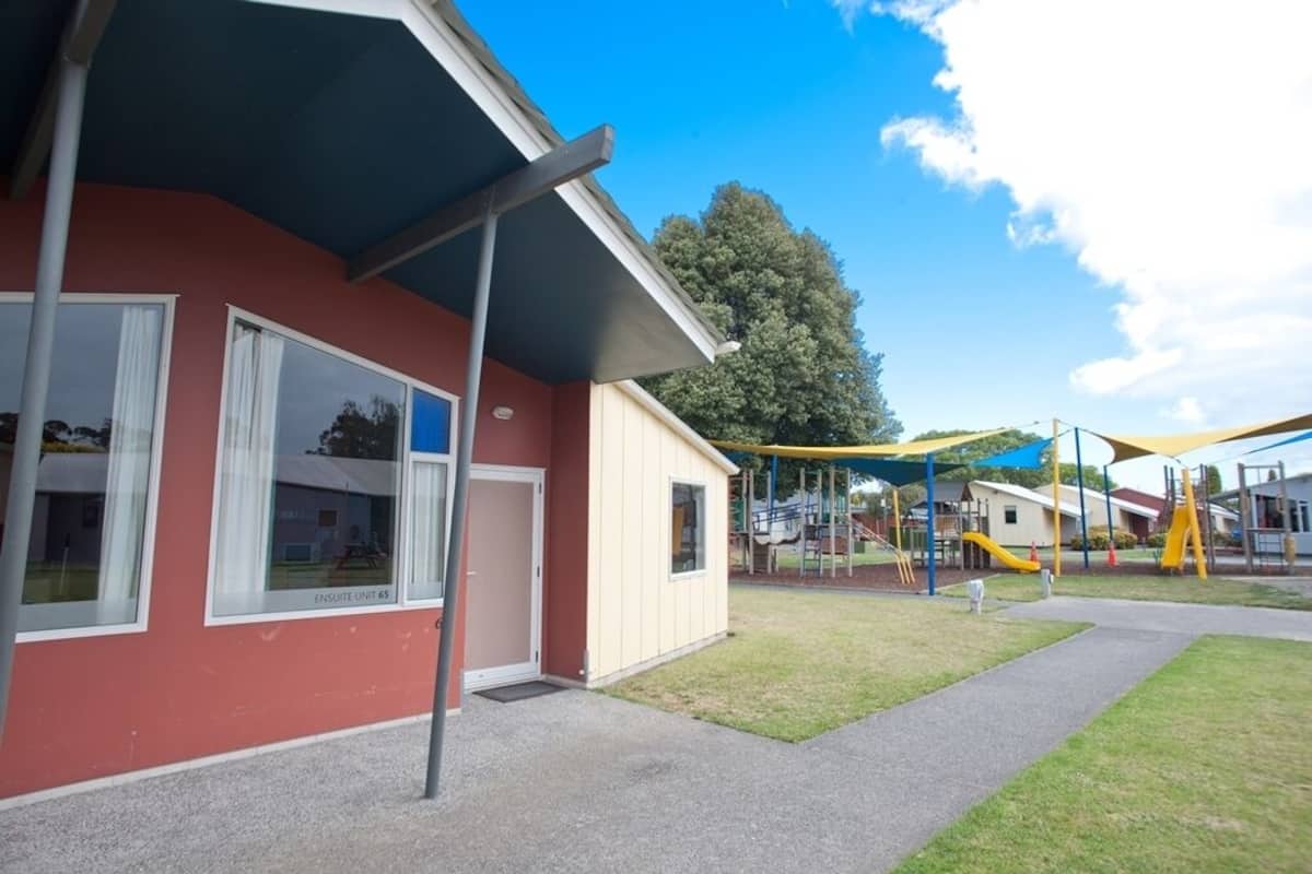 A building with a red exterior, large windows, and a covered outdoor area with playground equipment.