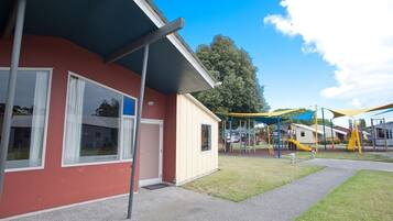 A building with a red exterior, large windows, and a covered outdoor area with playground equipment.