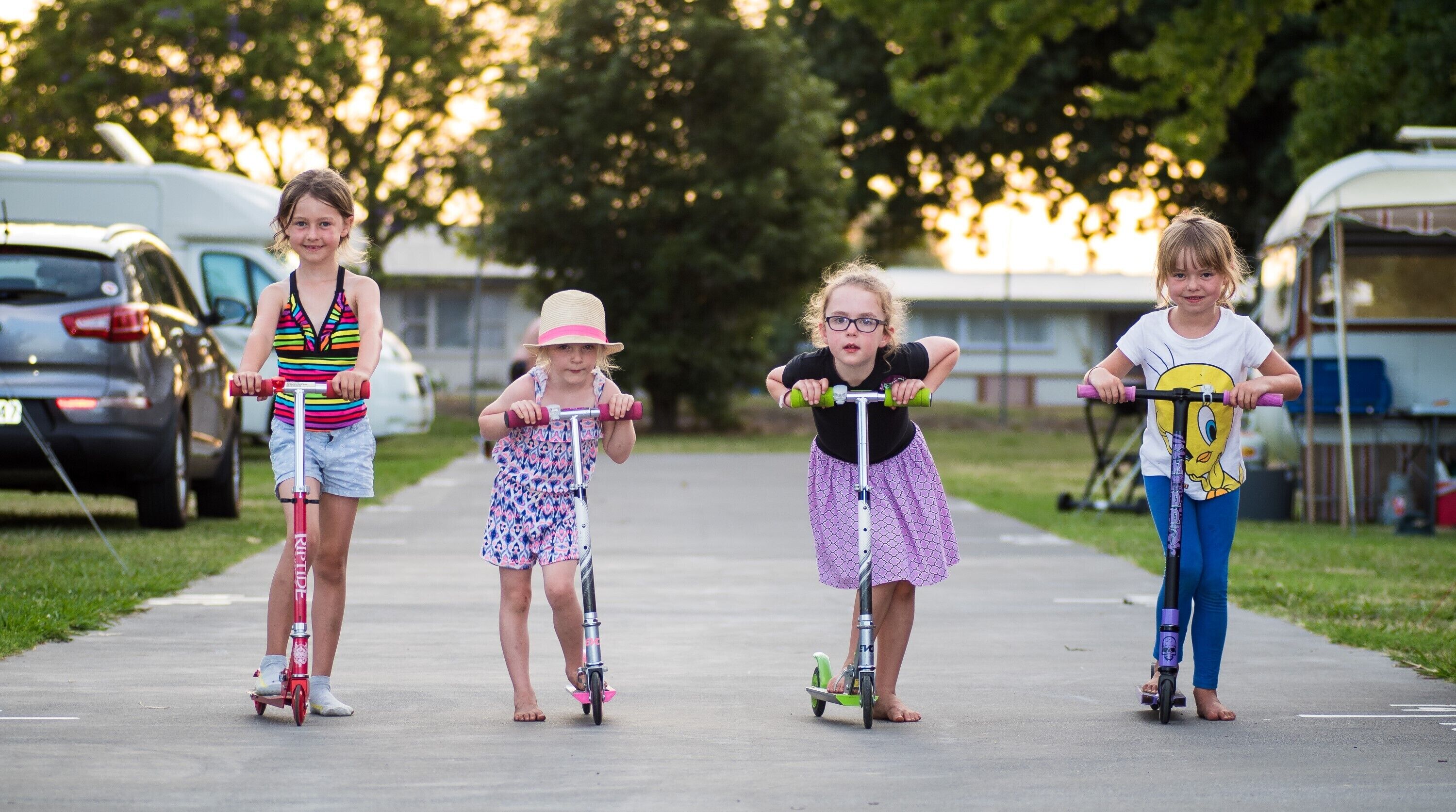 Four children riding scooters on a sidewalk.