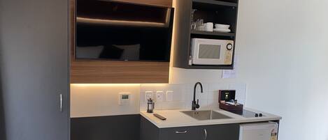 Una kitchenette compacta con microondas integrado, un lavamanos y un refrigerador pequeño.