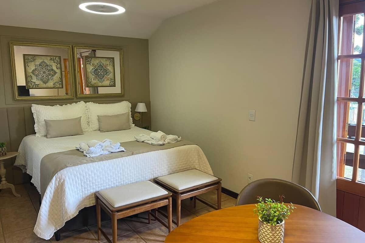 A hotel room with a bed, bedside tables, a round dining table with a plant, and a window with curtains.