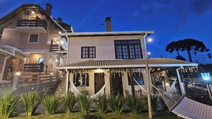 A two-story house with a balcony, a covered porch with string lights, and a hammock. - Pousada Flor de Lua Monte Verde (Camanducaia)