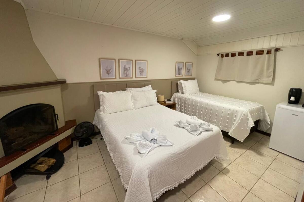 A hotel room with a bed, two bedside tables, a small refrigerator, a fireplace, and framed pictures on the wall.