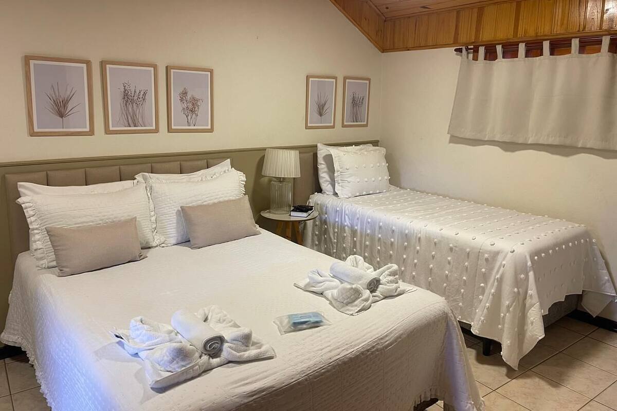 A hotel room with two beds, a nightstand, a lamp, and framed botanical artwork on the wall.