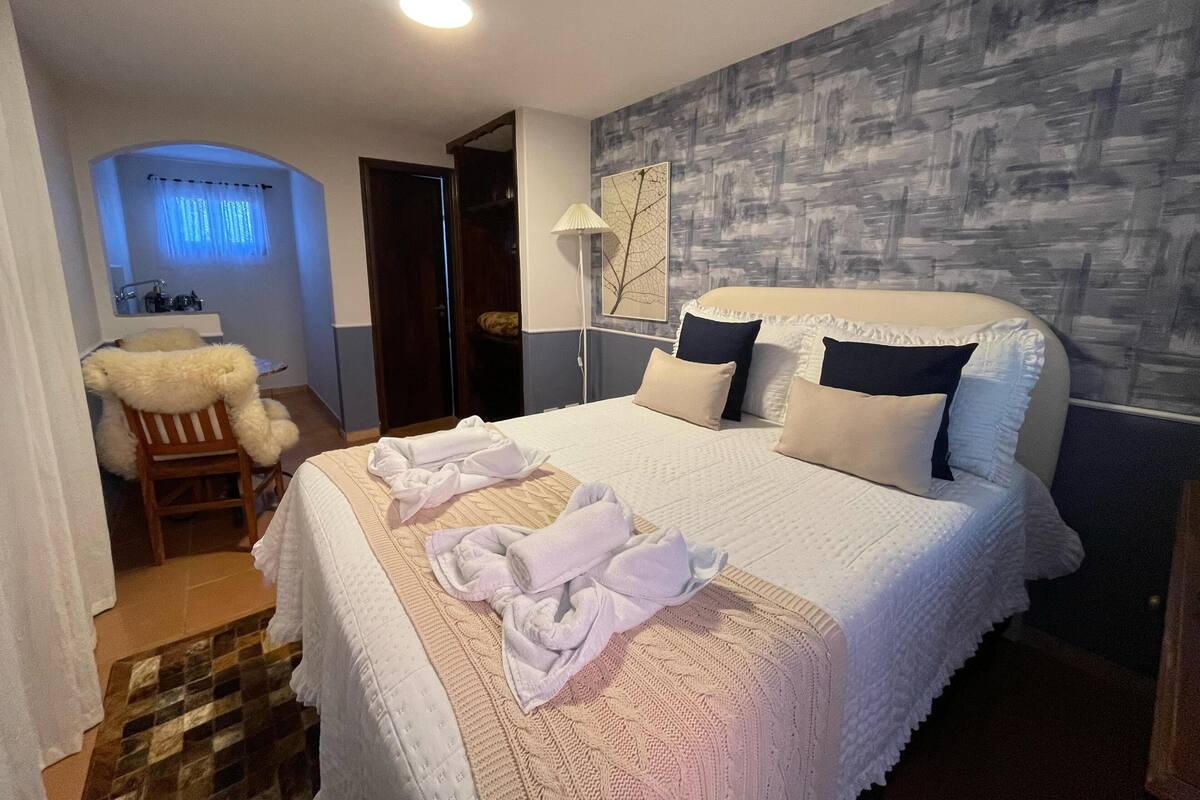 A hotel room with a large bed, a desk with a chair, a bathroom with a mirror, and a wall with a textured design.