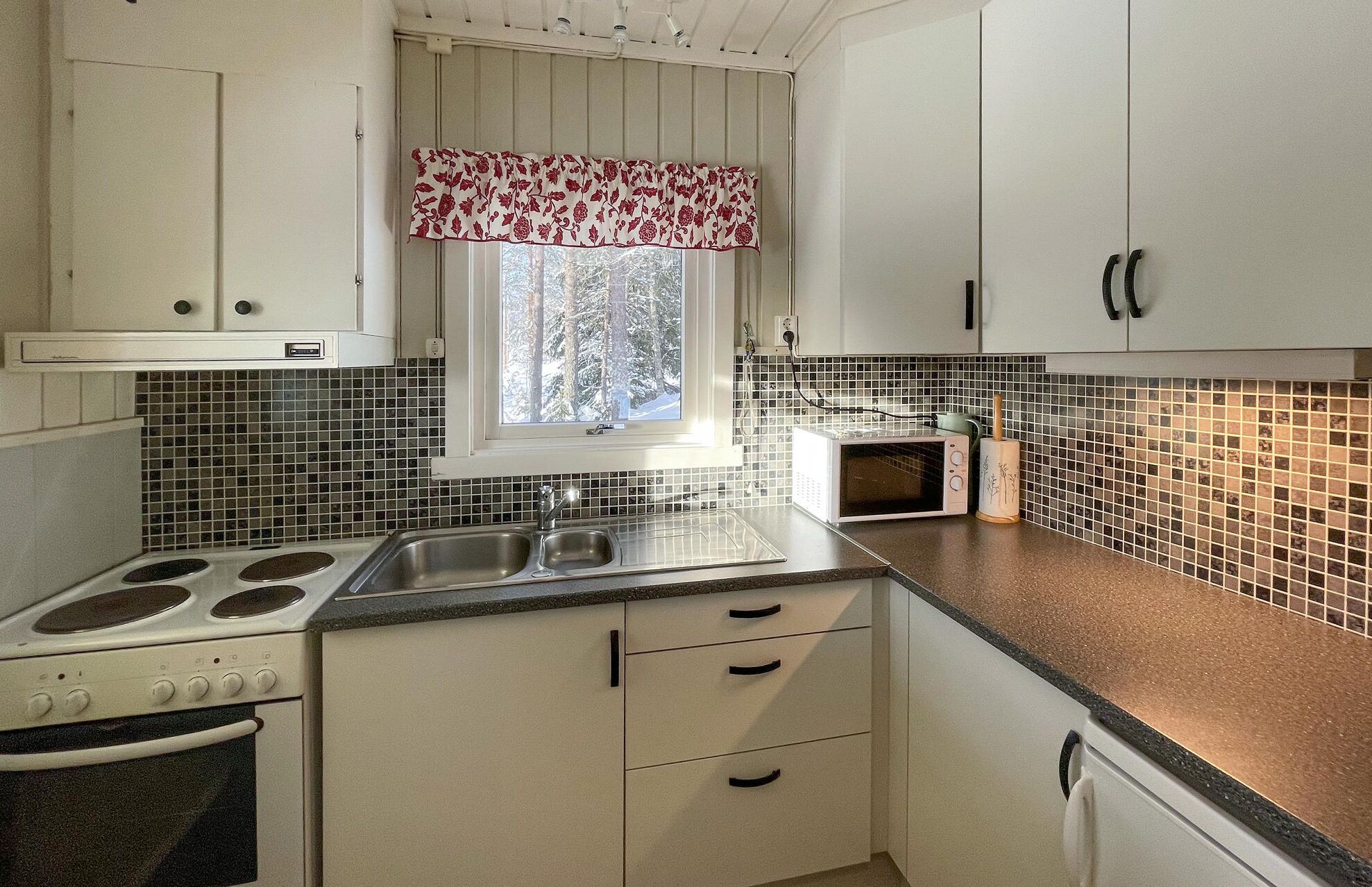 A kitchen with white cabinets, a stove, a sink, and a microwave.