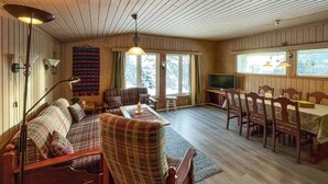Ein gemütliches Blockhaus-Interieur mit Sofa, Esstisch, Stühlen, Fernseher und Kamin.