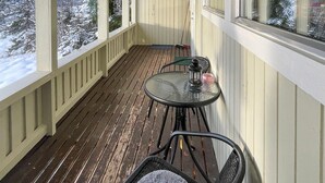 Eine Holzterrasse mit einem Glastisch und Stühlen, einem Laternenlicht und einem an der Wand angelehnten Besen.