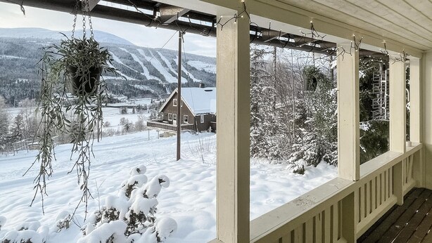 Eine überdachte Veranda mit Blick auf eine verschneite Landschaft, einschließlich eines Hauses und Bergen.