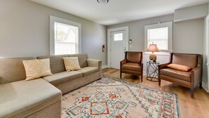 A living room with a beige sectional sofa, two leather armchairs, a patterned rug, and a door with a window. - Stunning Charlotte Retreat ~ 2 Mi to City Center! (Charlotte)