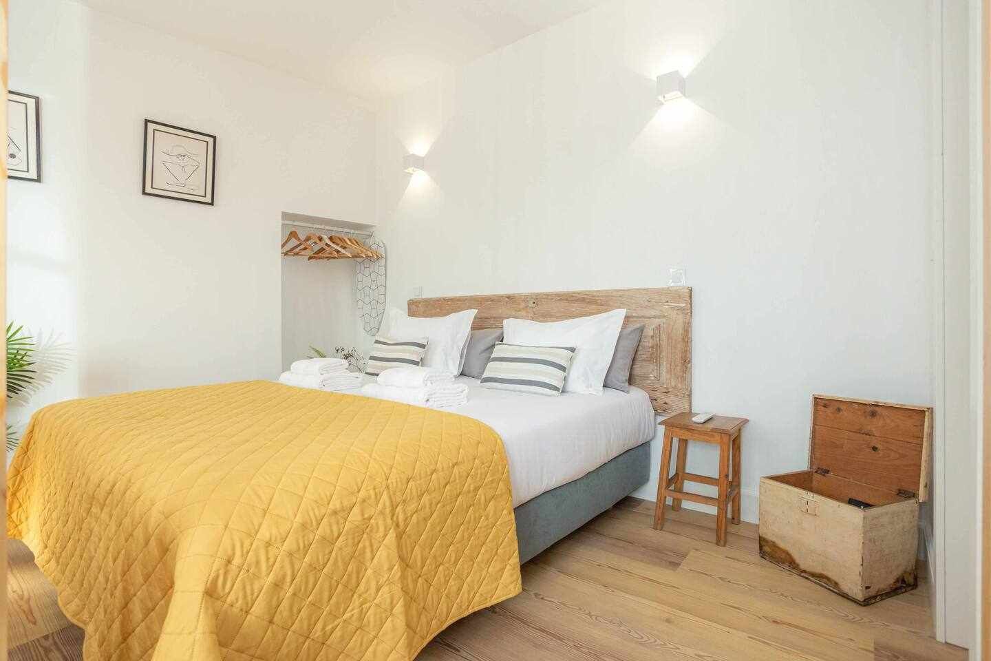 A bedroom with a bed, bedside tables, a wooden headboard, and a wall-mounted light fixture.