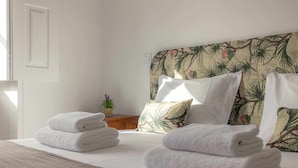 A neatly made bed with white towels, a floral headboard, and a small potted plant on a wooden nightstand. - Casas da Couraça - Camões (Coimbra)