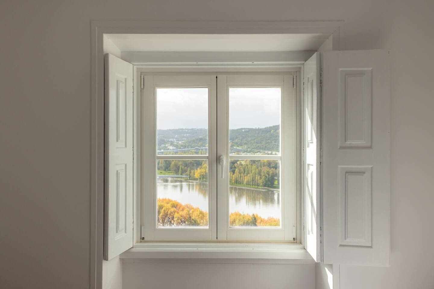 A room with a large window overlooking a lake and autumn foliage.