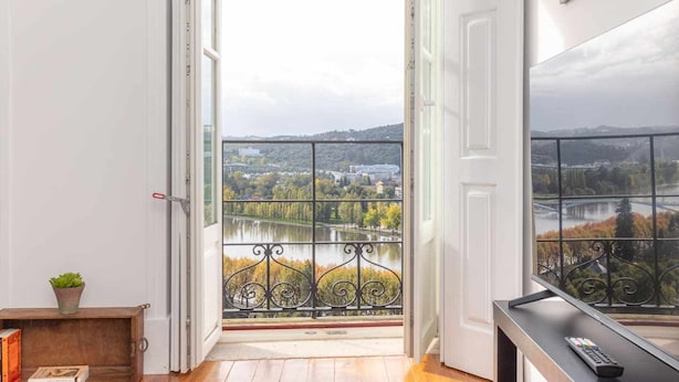 A room with a view of a river and hills, a balcony with a metal railing, and a wooden floor. - Casas da Couraça - Camões (Coimbra)