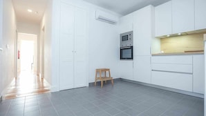 A modern kitchen with white cabinets, a microwave, and a wooden stool. - Casas da Couraça - Camões (Coimbra)