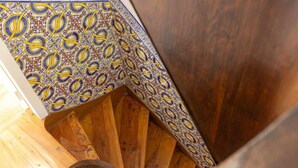 A wooden spiral staircase with ornate blue and yellow patterned tiles at the top. - Casas da Couraça - Camões (Coimbra)