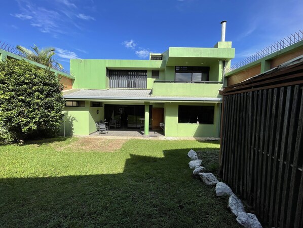 A modern two-story house with a green exterior, a covered patio, and a fenced backyard. - The Rainier Bed & breakfast (San José)