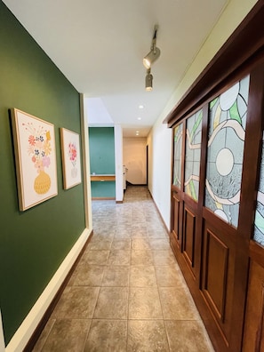 A hallway with green walls, tiled flooring, and framed floral artwork. - The Rainier Bed & breakfast (San José)