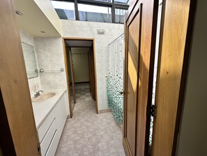 A narrow bathroom with a bathtub, a sink, and a shower area. - The Rainier Bed & breakfast (San José)