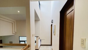 A narrow hallway with a wooden door on the right, a white wall with a light switch, and a tiled floor. - The Rainier Bed & breakfast  (San José)