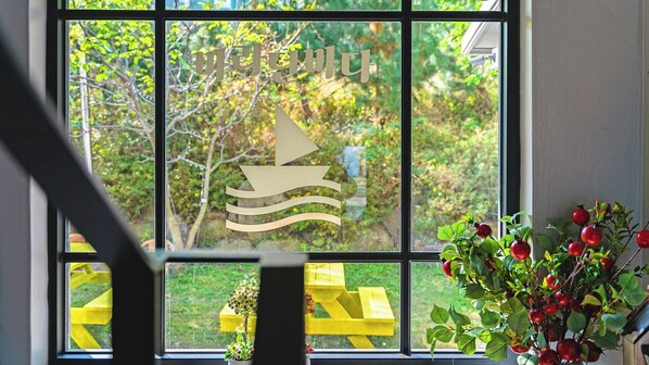 Ein Fenster mit einem Segelboot-Motiv, eine gelbe Bank davor und ein Blumentopf mit roten Beeren.