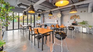A modern dining area with tables and chairs, overhead lighting, a clock, and a view of the outside. - Baradeon Bada Pension, Yangyang (Yangyang)