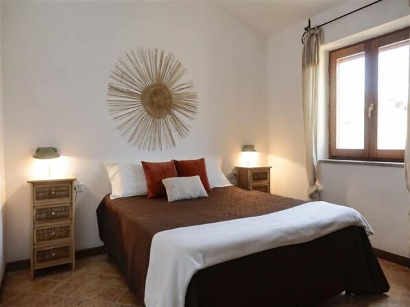 A bedroom with a large bed, two bedside tables, a wall-mounted decorative piece, and a window with curtains.