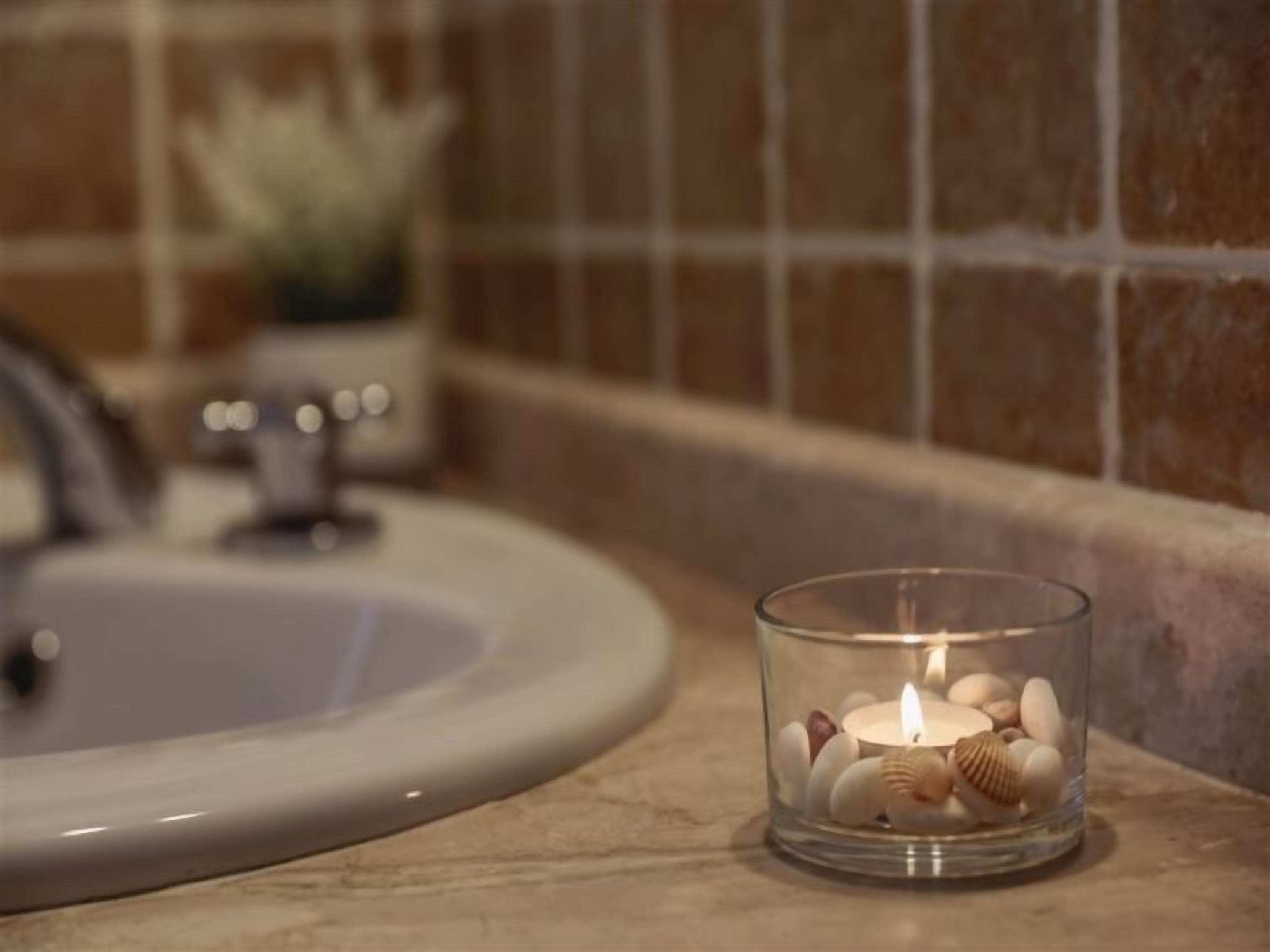 Ein Badezimmerwaschbecken mit einem Glas-Kerzenhalter, der Kerzen und dekorative Steine enthält.