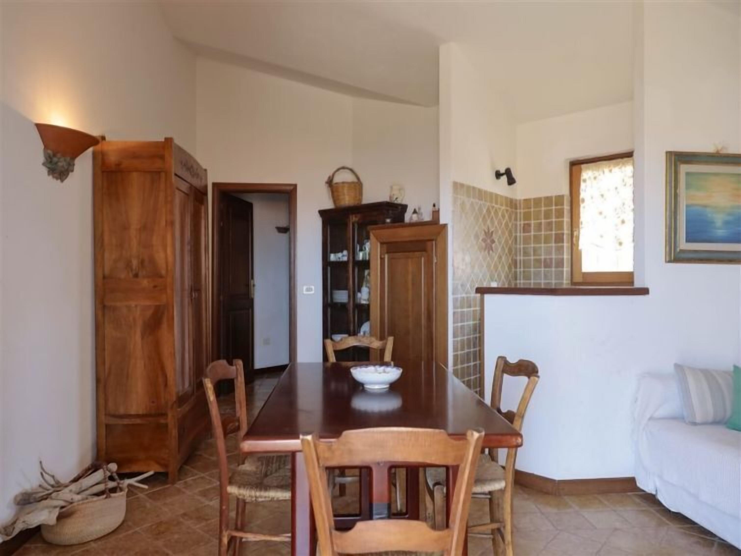 A dining area with a wooden table and chairs, a cabinet with dishes, and a window with a view.